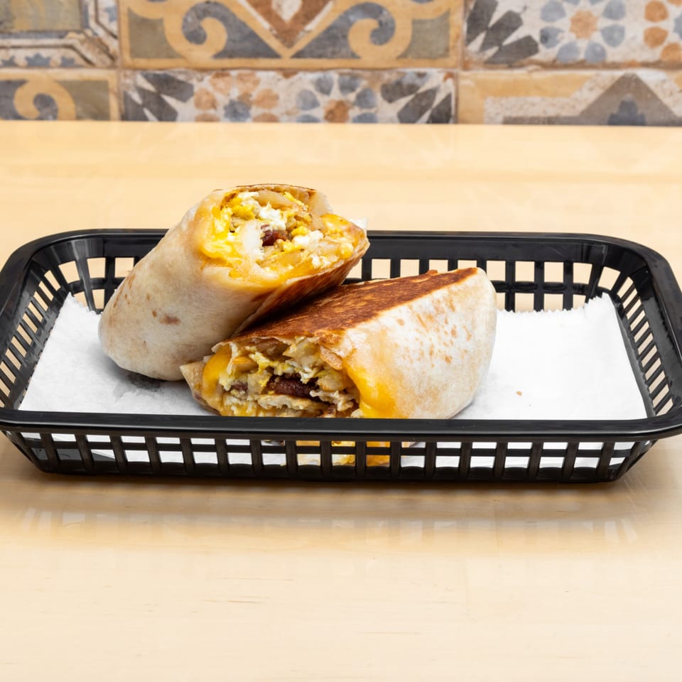 Two breakfast burritos, one cut in half, filled with eggs, cheese, and sausage in a black basket.